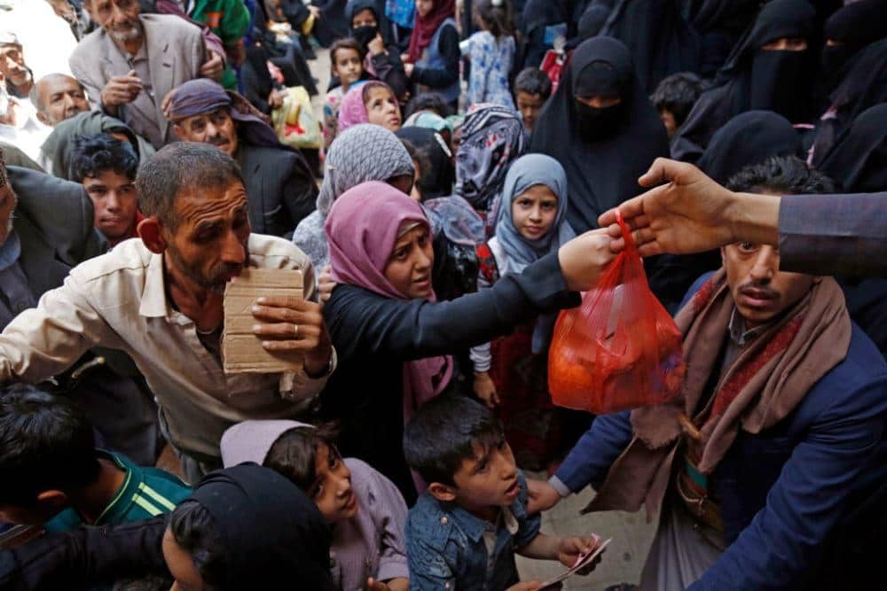 Yemen aid distribution, a man receives a red plastic bag of food, supporting crisis relief efforts via crypto donations like Ethereum.
