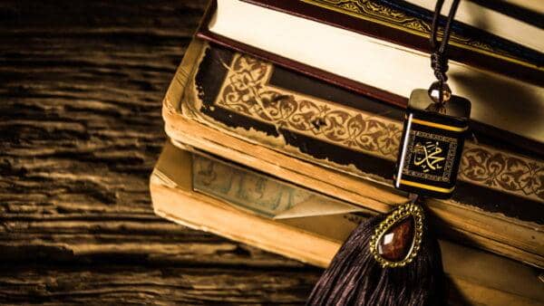 A stack of Islamic books including the Quran and Hadith, with a decorative Islamic pendant. Support Muslim relief efforts with BTC donations for charitable giving.