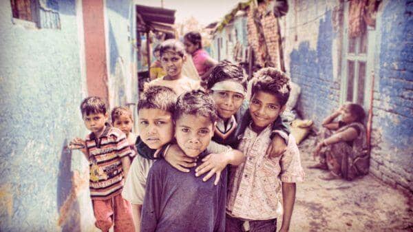 A group of children stand in a narrow alley with distressed buildings. One child in front wears a purple shirt, another a striped shirt. Crypto donations enhance aid, with USDT facilitating support.