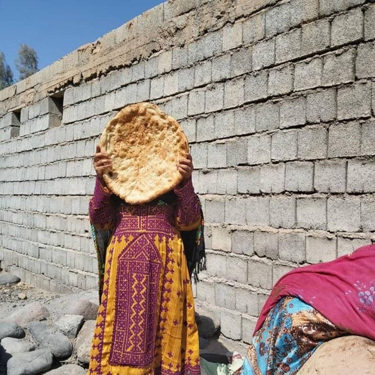 A woman in traditional clothing holds flatbread in front of her face. This symbolizes the need for basic supplies and aid for women in crisis, supported by crypto donations like SOL.