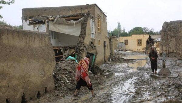 Damaged homes in Afghanistan with people walking through mud, symbol of need for humanitarian aid and crypto donations via USDT.