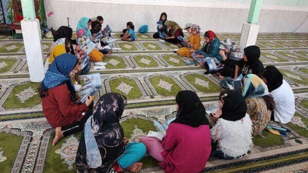 Children sitting on a carpeted floor, reading books. Donation for education is facilitated by crypto, with ongoing rewards achieved through Halal Crypto Giving via platforms like RLUSD.
