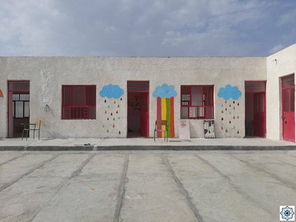 Exterior of a colorful school building with painted clouds and raindrops above windows; cheerful mural signifies hope for children acquiring education through crypto donations, processed via USDT.