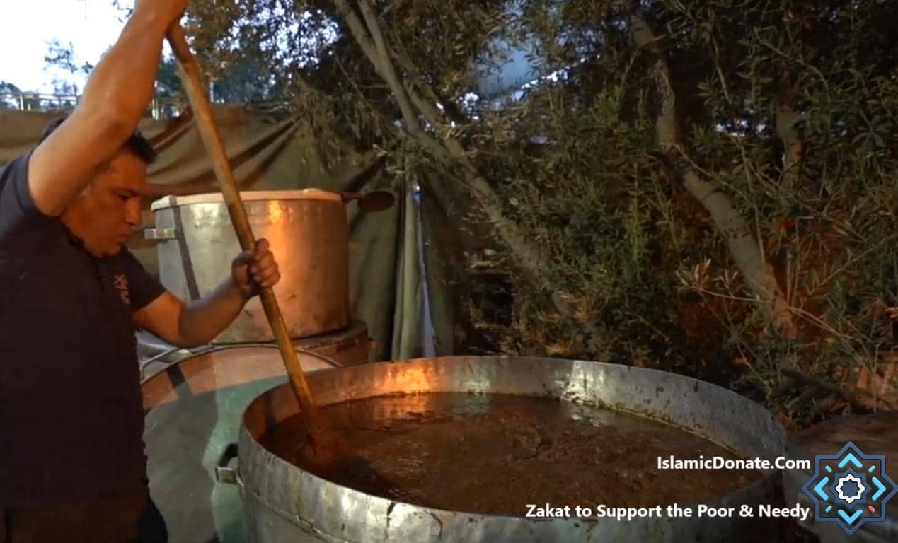 A man stirs a large pot of food, preparing a charitable meal. This charitable effort can be supported by crypto donations like Bitcoin.