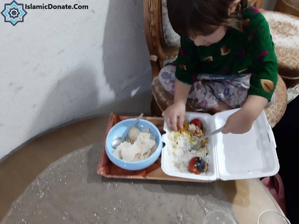 A child eats rice with tomatoes from a take-out container; rice is also in a blue dish. This act of giving is facilitated by IslamicDonate.com and supports crypto donations like BTC, providing nourishment for those in need as part of Aqiqah Qurbani for newborn babies.