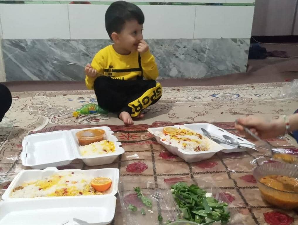 A child sits on a carpeted floor, looking away from the camera, with takeaway containers of rice and sauce in front of him. These meals are part of an Aqiqah Qurbani donation, facilitated by Bitcoin, which provides food for the needy.