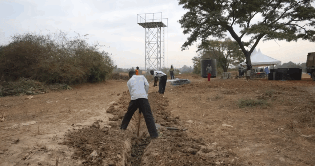 Workers digging a trench near a water tower, symbolizing construction of a water well and crypto donations like BTC funding community development and Sadaqah Jariyah.