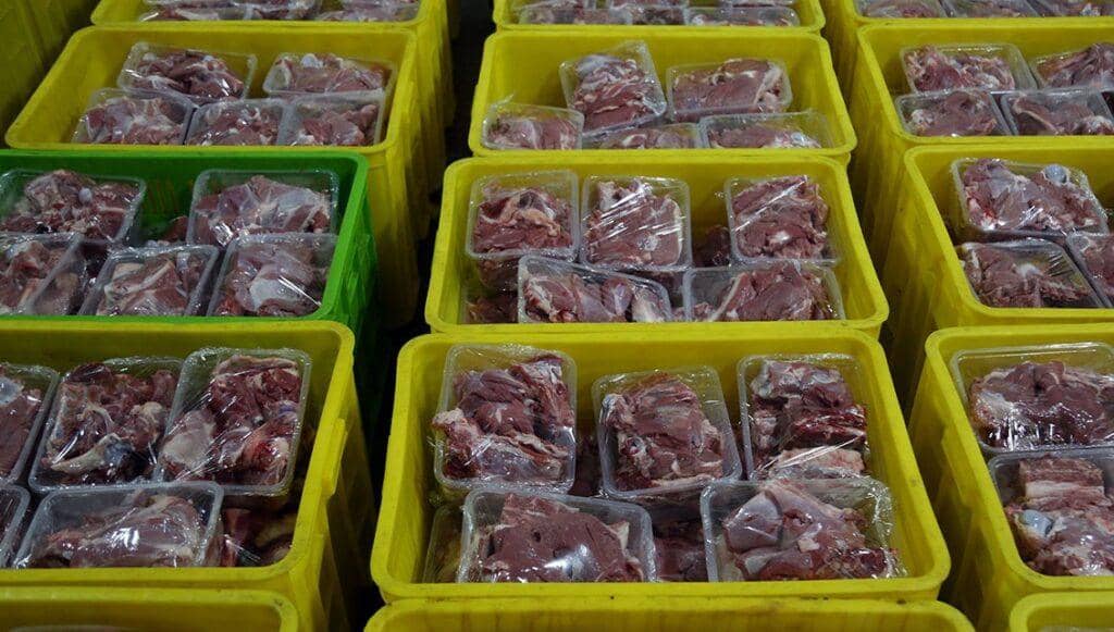 Rows of yellow bins filled with pre-packaged raw meat portions, ready for distribution as Eid al-Adha charity, supported by USDT donations for sustenance relief.