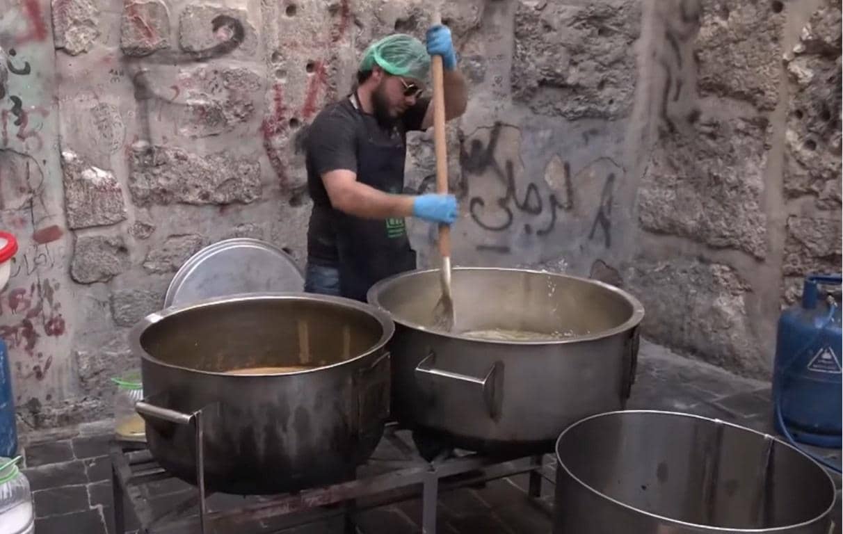 Man stirring large pot of food, preparing meals with crypto donation, fidya, Ramadan obligation, feeding the ummah, powered by SOL.