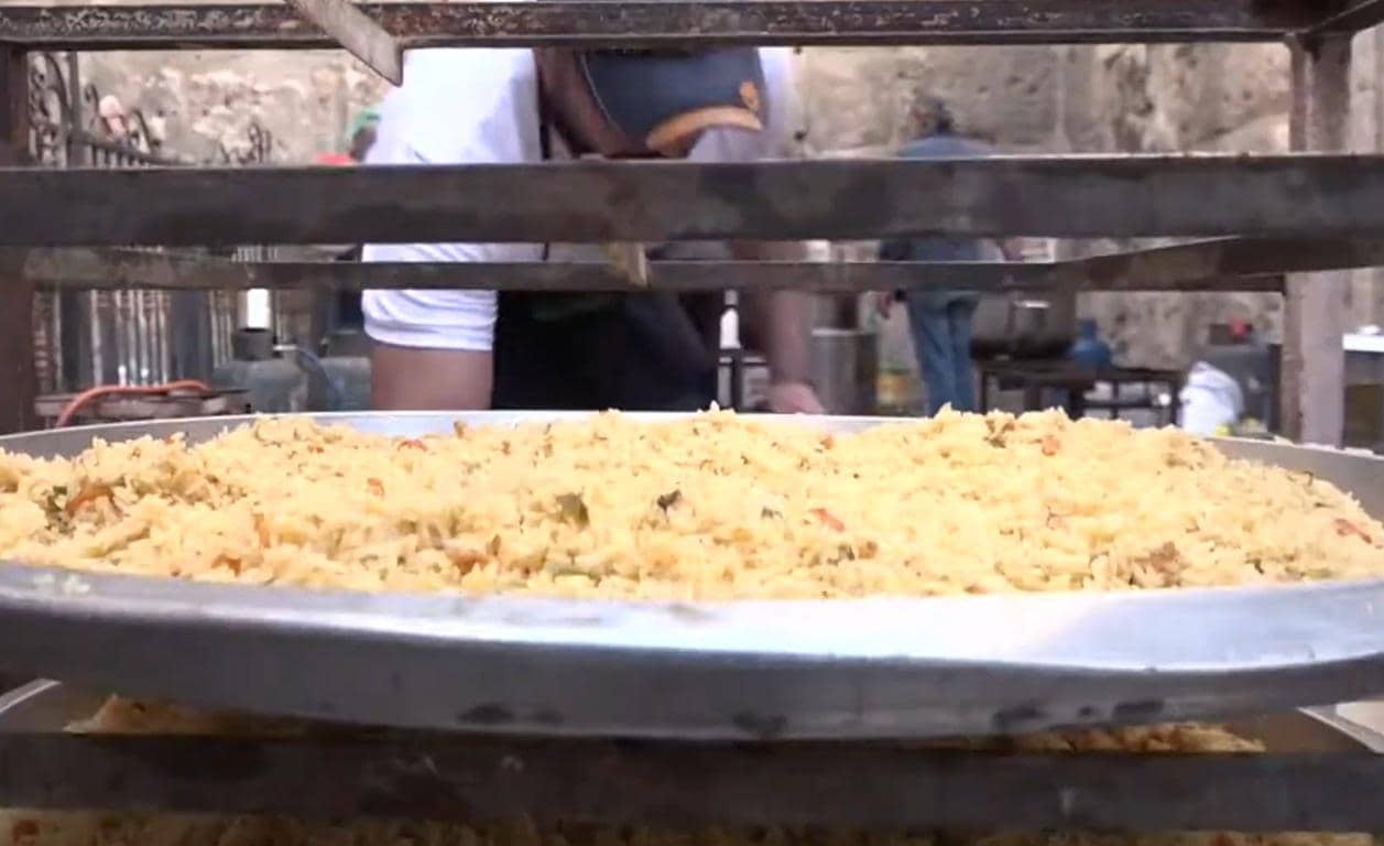 Large tray of rice dish being prepared for distribution, with crypto donation implied via SOL, supporting fidya and charity for the Muslim community.