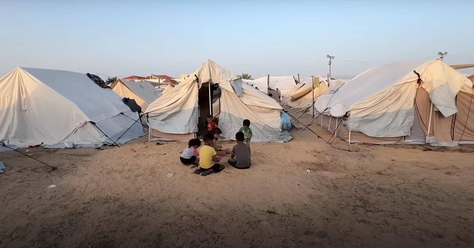 Children playing in front of refugee tents in Palestine, aid delivered via ETH. Keywords: Palestine aid, delivering hope, children's education, overcoming challenges, humanitarian crisis.