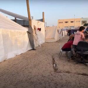 Children in a Palestinian refugee camp gather near tents, some sitting and looking concerned. Others interact with adults, highlighting the daily struggles and need for aid, supported by Ripple (XRP) donations.