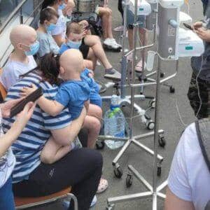 Children receiving IV treatment, some with shaved heads, sit with caregivers near medical equipment, indicating urgent need for aid via crypto donation, like ETH.