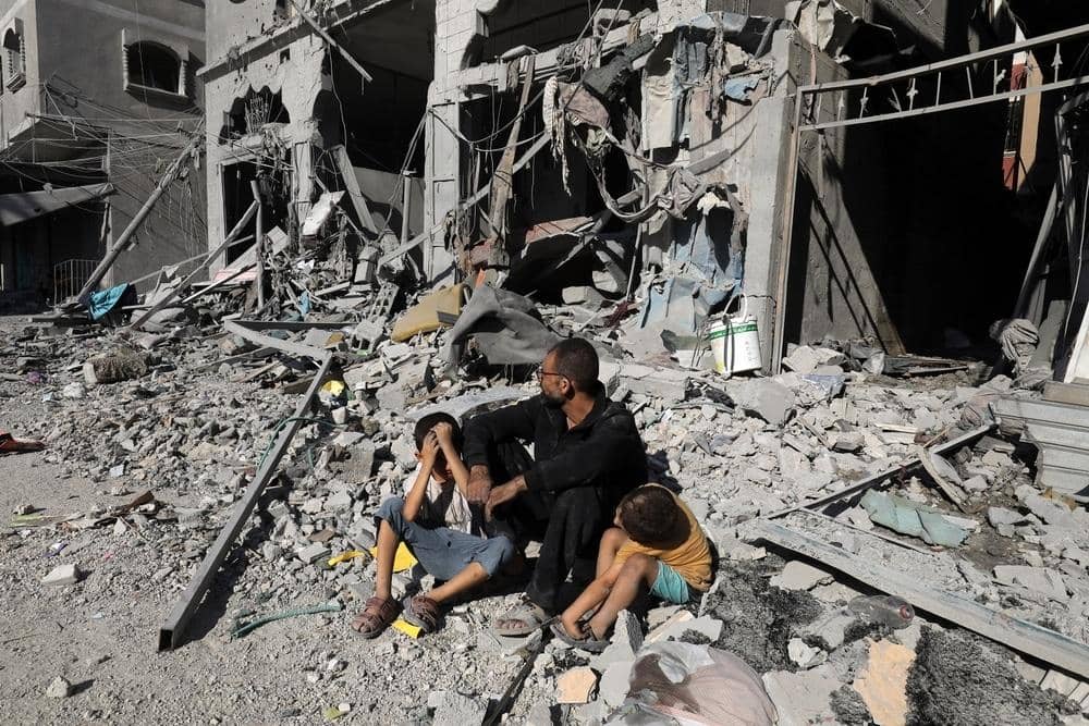 A father sits with his two distressed children amidst rubble and destroyed buildings, symbolizing the devastating impact of conflict. Crypto Zakat donations, including ETH, provide vital aid and support to families in need in Palestine.