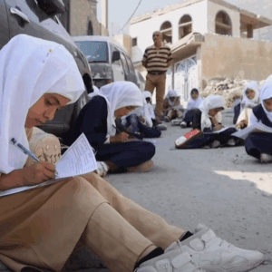 Children in hijabs learning outdoors, with one girl in the foreground writing, receiving crypto donation support via USDT, symbolizing educational aid for orphans.