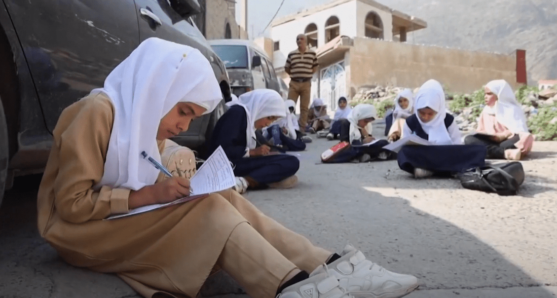 Children in hijabs learning outdoors, with one girl in the foreground writing, receiving crypto donation support via USDT, symbolizing educational aid for orphans.