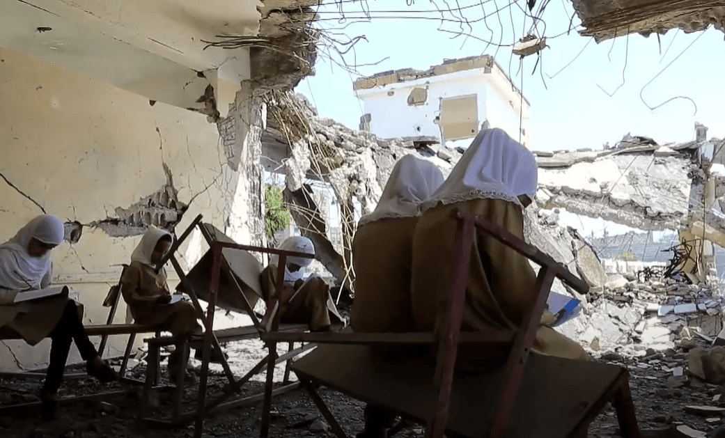 Children studying amidst destroyed classrooms, a testament to resilience empowered by crypto donations like BTC, reflecting the 49 orphans sponsored in the 2023-2024 academic year.