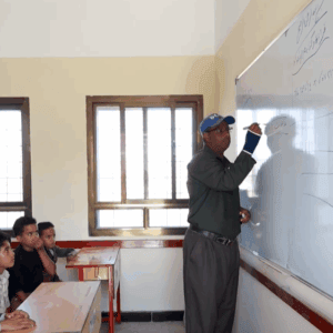 Sponsor of orphans classroom with teacher writing on whiteboard, crypto donations enable education for 49 children sponsored via ETH.