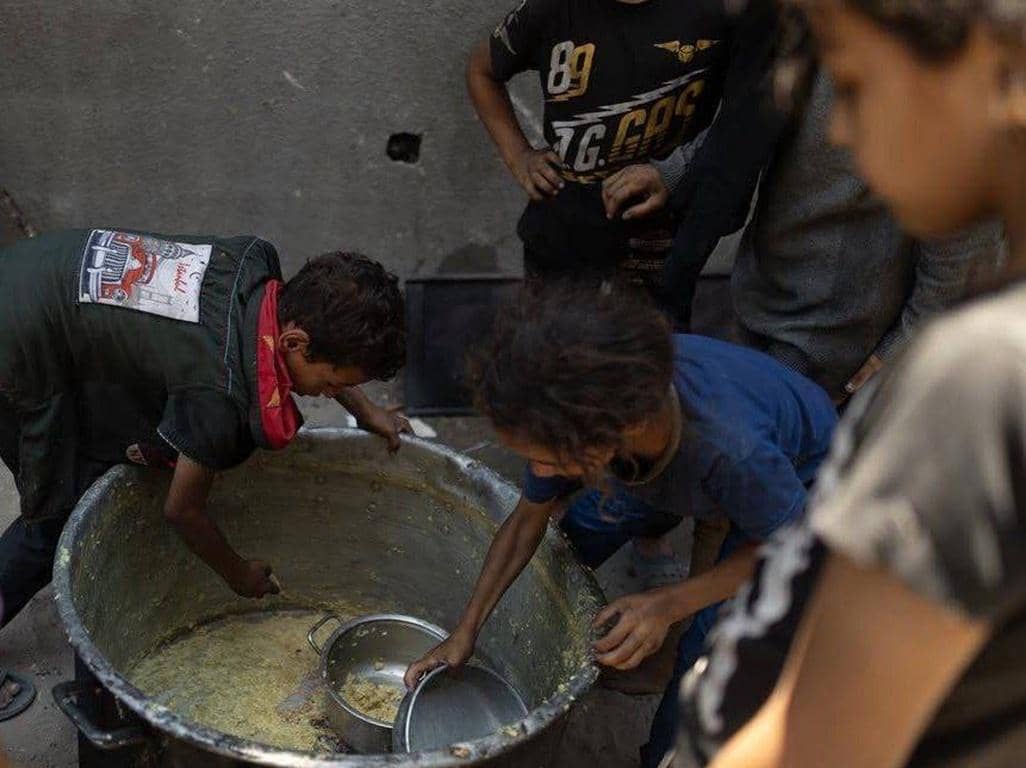 Children receiving Iftar meals from a large communal pot, highlighting the critical need for food aid in war zones like Gaza and Palestine, supported by crypto donations via BNB.