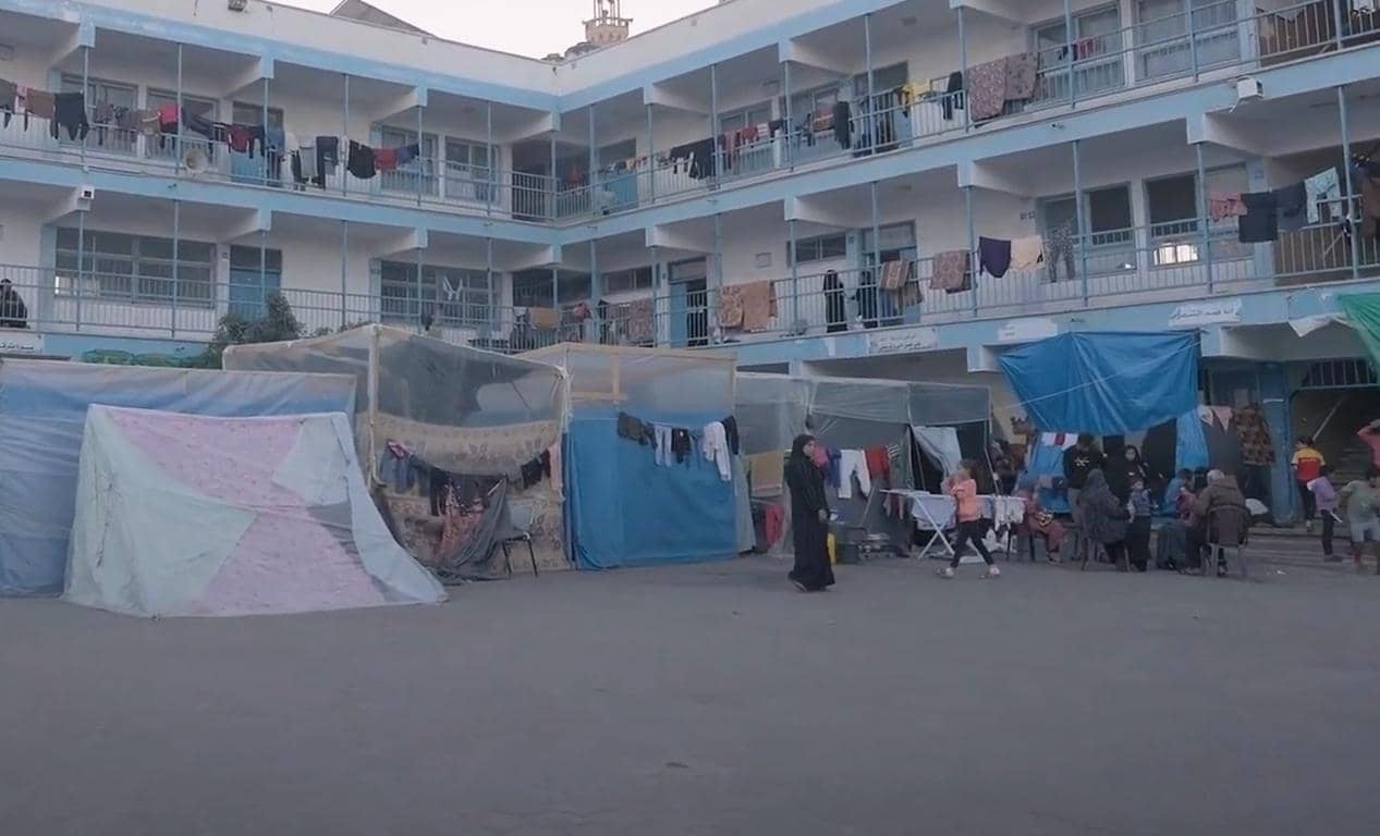 Makeshift shelters and tents set up in the courtyard of a building, with laundry hanging on lines. People are gathered in small groups. Supports crypto donations for Ramadan Iftar in Gaza, Palestine and Yemen, facilitating essential aid with BTC.