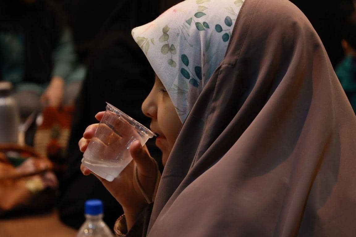 A young girl in a hijab drinks water from a plastic cup, symbolizing relief and sustenance provided through crypto donations for Ramadan iftar.