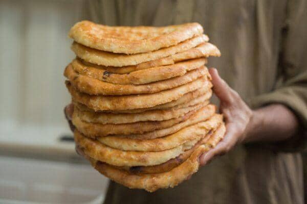 A person holds a tall stack of freshly baked unleavened flatbreads, prepared by Our Islamic Charity for the Feast of Prophet Muhammad 2024, with offerings supported via ETH.