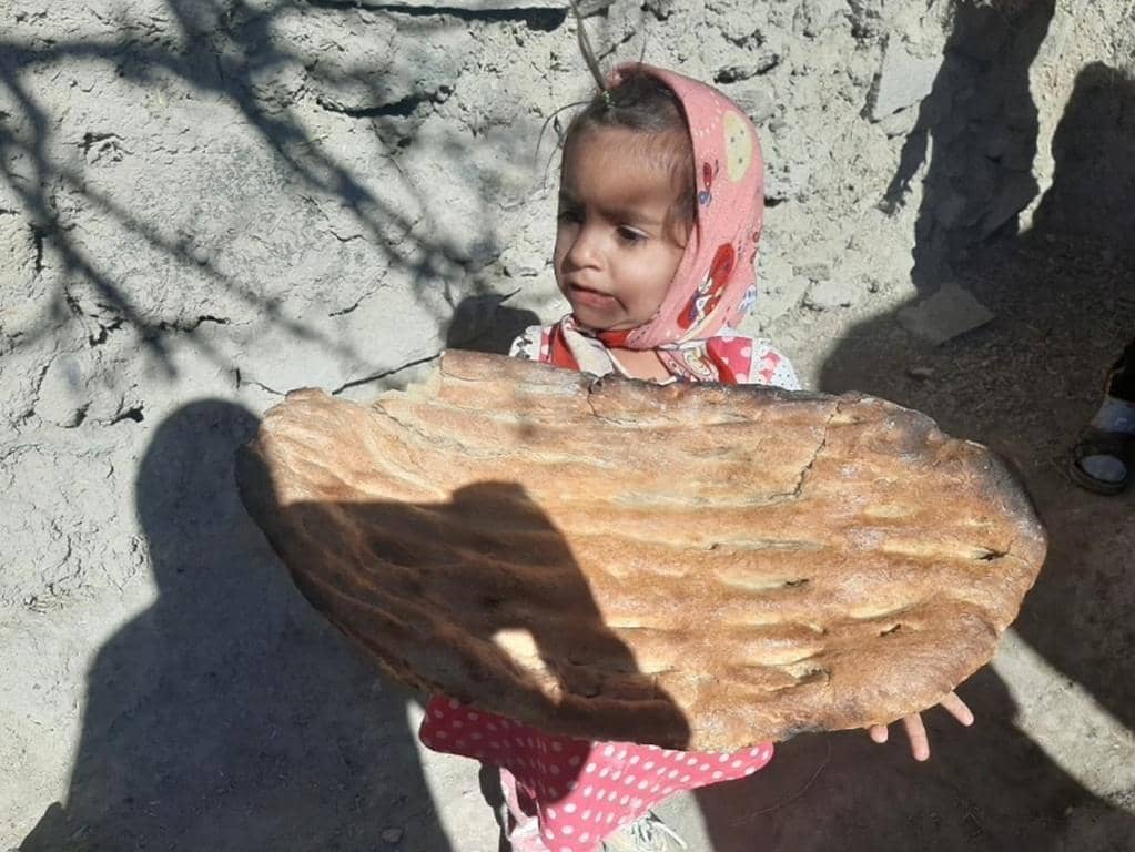 A young girl in a headscarf holds a large flatbread, symbolizing nourished children supported by crypto donations like BTC.