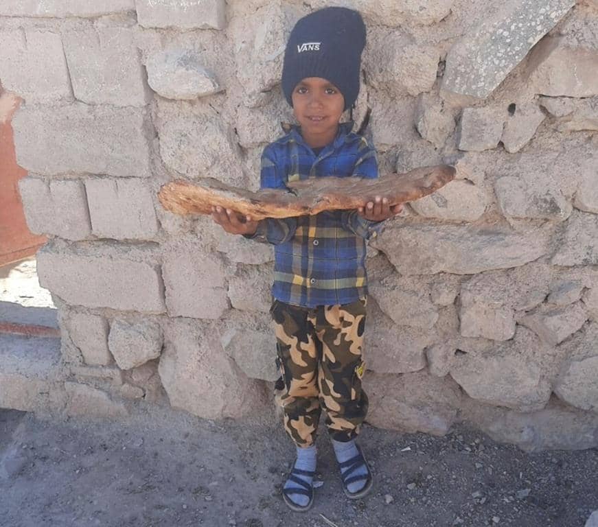 Young boy smiling, holding a large flatbread in front of a stone wall, symbolizing the blessings of crypto donations for Mawlid.