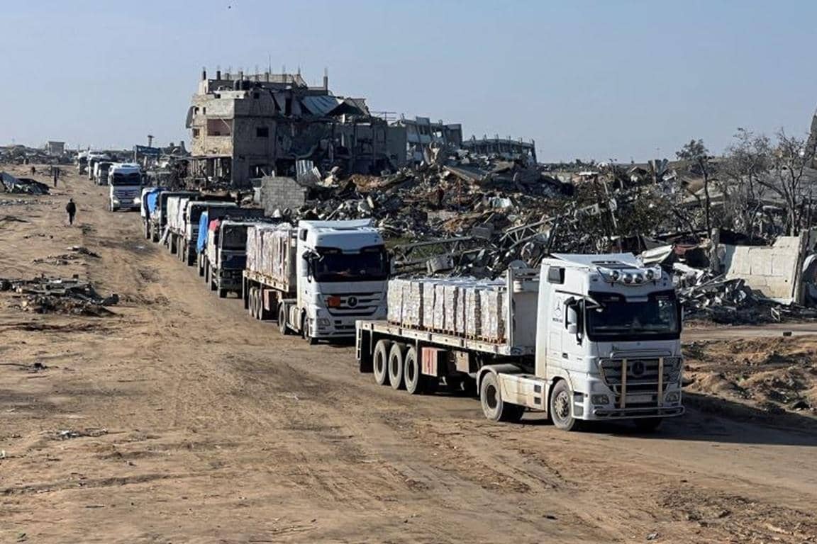 A convoy of aid trucks carrying supplies drives through a destroyed area in Gaza, implying crypto donations like PayPal USD support this humanitarian effort.