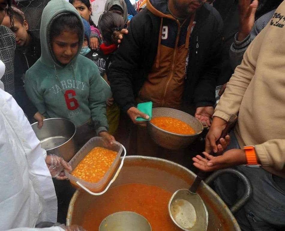 Children and adults receiving portions of food from a large communal pot, highlighting humanitarian aid efforts in Gaza, supported by crypto donations via AED.