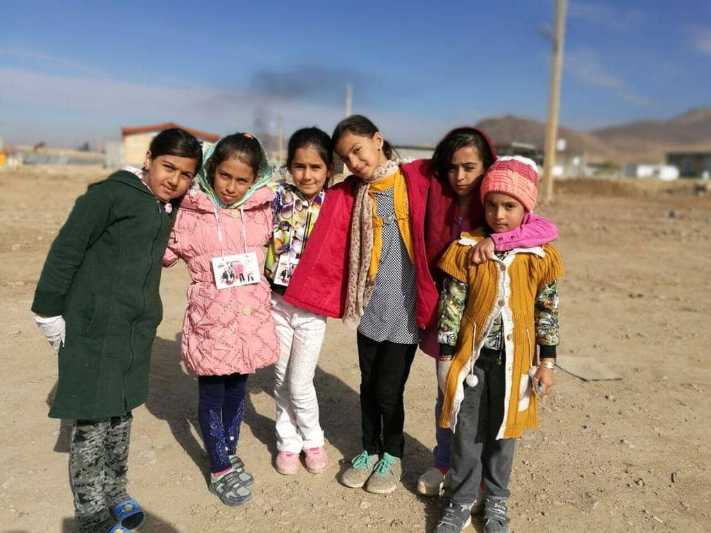 Six young girls in winter clothing pose together, their faces hopeful. Crypto donations provide warm clothes, shelter, and heating for displaced families in conflict zones, bringing warmth and mercy this winter via DOGE.