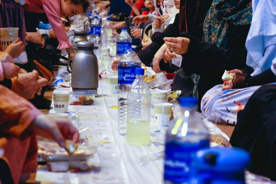 Group of people sharing an iftar meal, with food and drinks laid out on a table, implying the generous distribution of aid through crypto, possibly BTC, to those in need during Ramadan.