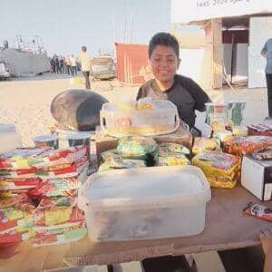 A smiling boy works at a stall selling food and snacks, Universal Children's Day focus on working children, with donations supported by BTC.