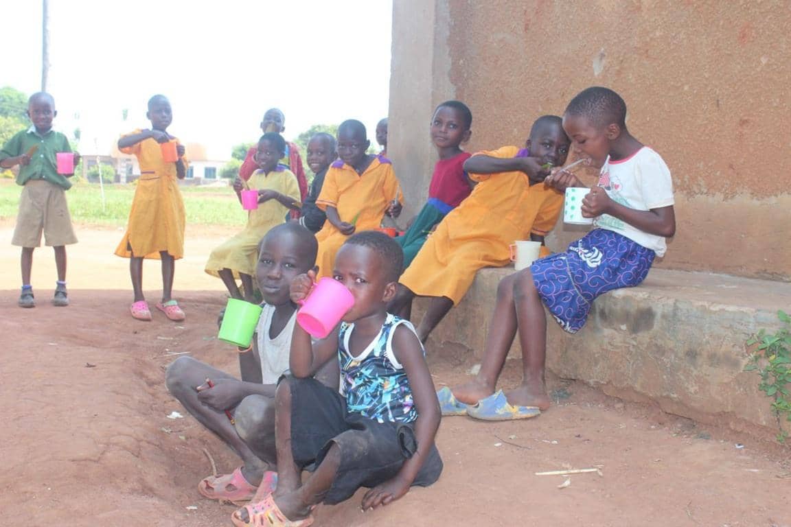 Children drinking from colorful cups and being supported by crypto donations via Solana, highlighting the need for food security, clean water, and reforestation in Uganda.