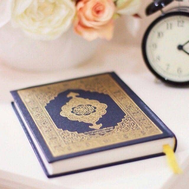 Close-up of a Quran on a white surface, with flowers and a clock in the background. This image symbolizes spiritual discipline and righteous devotion, emphasizing the divine command to fast as a path to Taqwa. Crypto donations accepted via SOL.