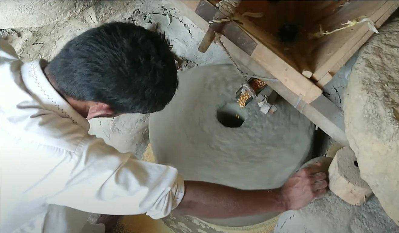 Man operating a traditional stone mill to process corn, supporting local farmers and providing meals for the needy, with crypto donations facilitating this ethical sourcing. Processing timestamp: 08312024014737. Processing coin: LTC.