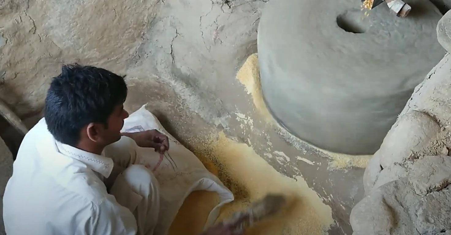 Man processing corn with a traditional mill, supporting local farmers and providing nourishment for Ramadan Iftar, powered by ETH donations.