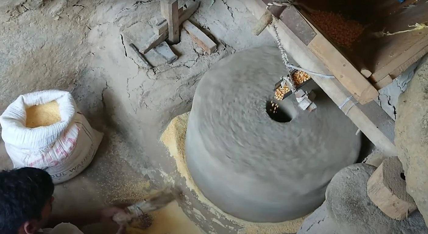 Local farmer using manual mill to process corn into flour for Ramadan meals, supported by crypto donations via XRP.