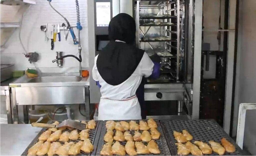 A cook in a hijab prepares food for the needy at a soup kitchen, likely supported by BTC donations, serving the Muslim Ummah with dedication and faith.