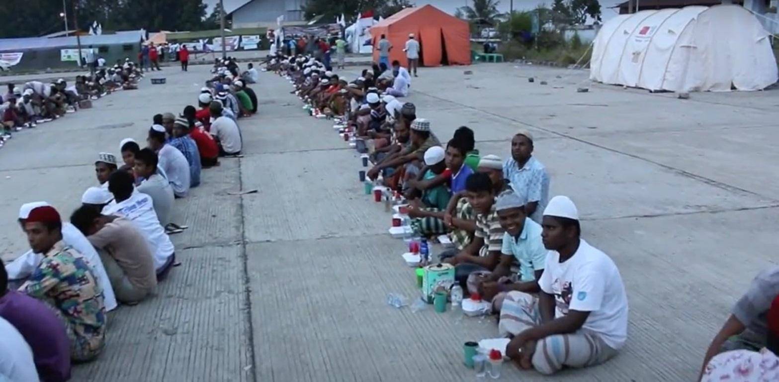 Muslims sit in rows to receive Iftar meals, with food packages and sustenance provided by donors, including crypto contributions like LTC.