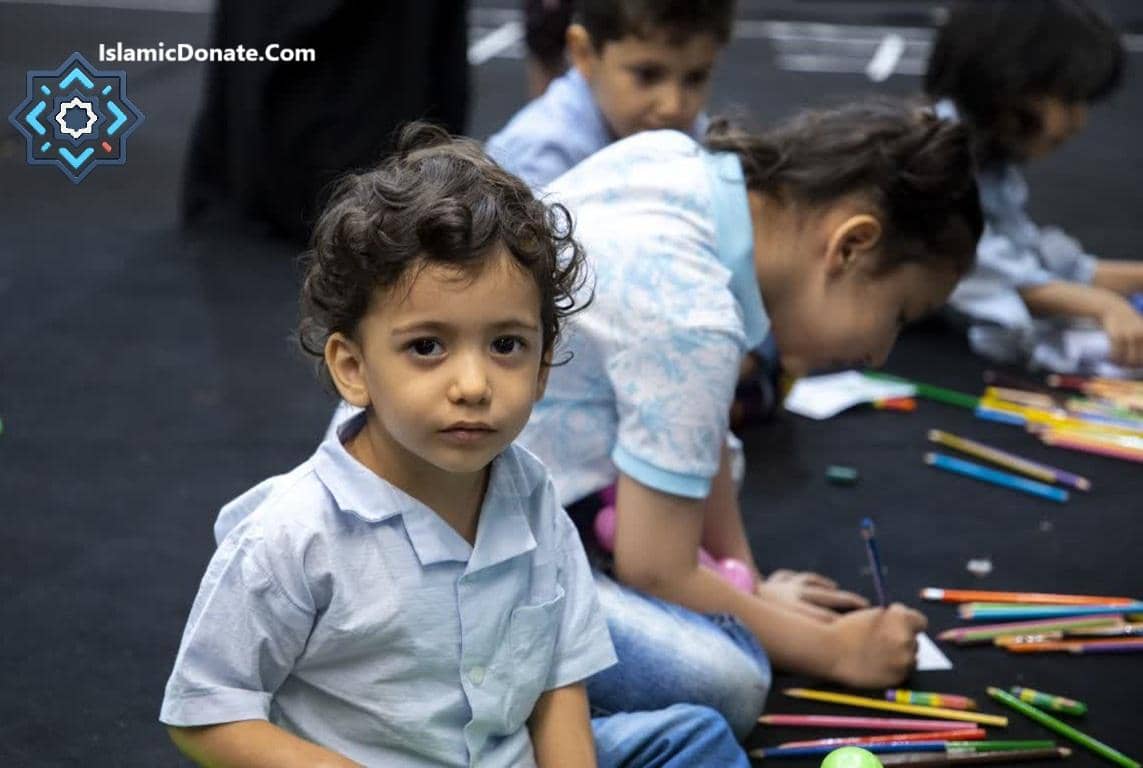 Young boy looking at the camera with other children drawing in the background, symbolizing support for Palestinian children through crypto zakat donations.