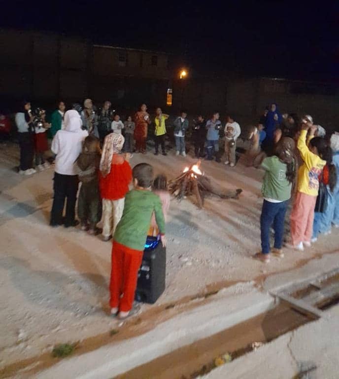 A diverse group of children and adults gathered around a bonfire at night, symbolizing community and warmth. Their gathering, supported by cryptocurrency donations like Bitcoin, represents hope and resilience in Palestine, offering sustenance and dignity.