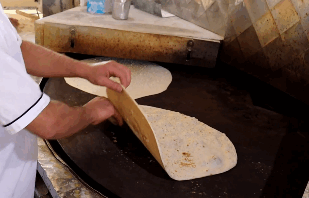 A baker prepares fresh bread on a large, circular griddle, symbolizing hope and sustenance for Palestine, with donations enabling cryptocurrency contributions like BTC.