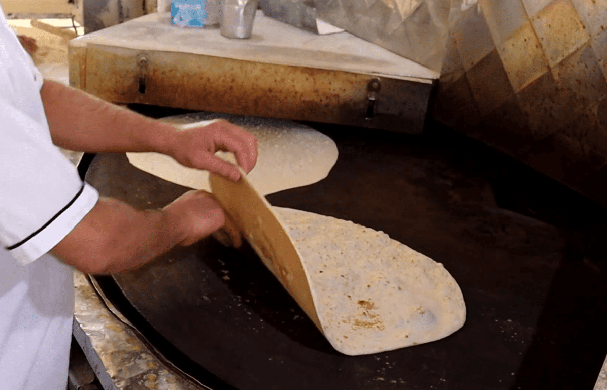 A baker prepares fresh bread on a large, circular griddle, symbolizing hope and sustenance for Palestine, with donations enabling cryptocurrency contributions like BTC.