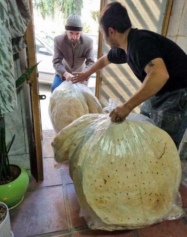 Two men hand large bags of flatbread to each other, symbolizing the provision of sustenance and hope to Palestinians, facilitated by cryptocurrency donations such as Bitcoin.