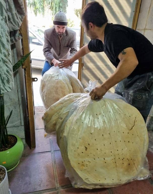 Two men hand large bags of flatbread to each other, symbolizing the provision of sustenance and hope to Palestinians, facilitated by cryptocurrency donations such as Bitcoin.
