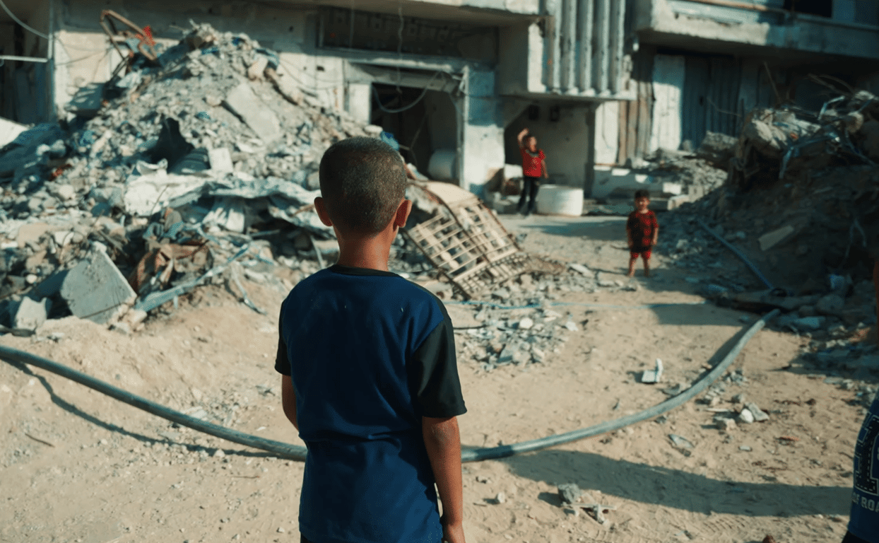 Child in foreground looks at rubble; two children play near destroyed buildings, symbolizing hope for aid via anonymous crypto donation with Bitcoin.
