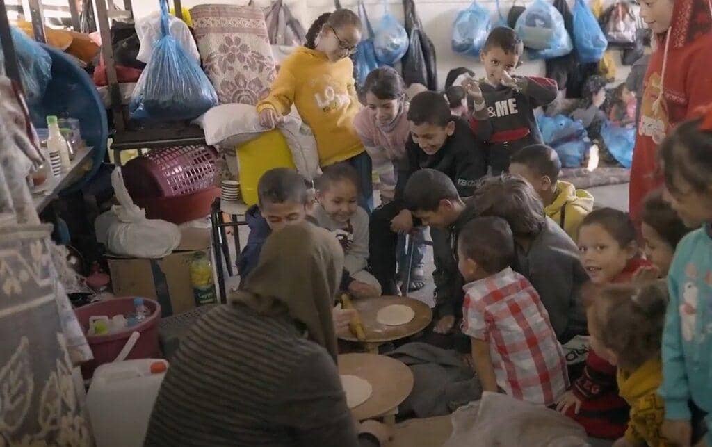 Children gather around as a woman prepares dough for bread, a scene of hope delivered by humanitarian aid supported by ETH donations.