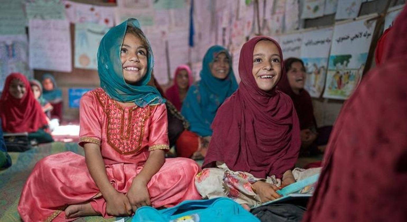 Two young girls in hijabs smile brightly while sitting in a classroom . They are learning, with crypto donations supporting their education.