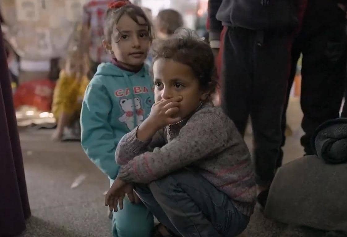 Two young children, one crouching with a hand over her mouth, the other standing, hinting at vulnerability and hope in the context of anonymous crypto donations via Bitcoin.